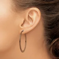 A person wearing a pair of simple oval hoop earrings in a polished silver-toned metal, shown from the side view of their ear and neck.