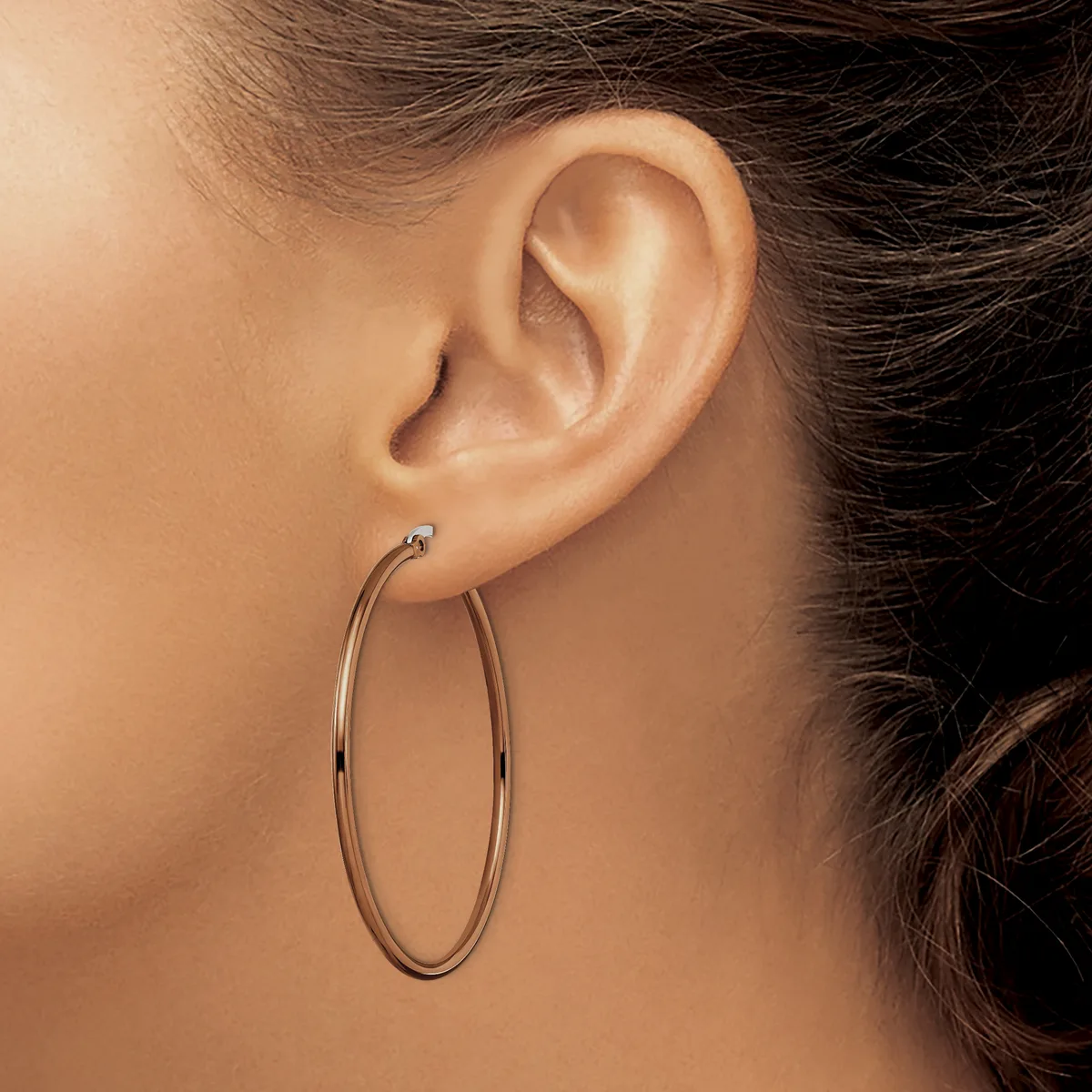 A woman wearing a pair of large oval hoop earrings in a polished metallic finish, shown from the side profile.