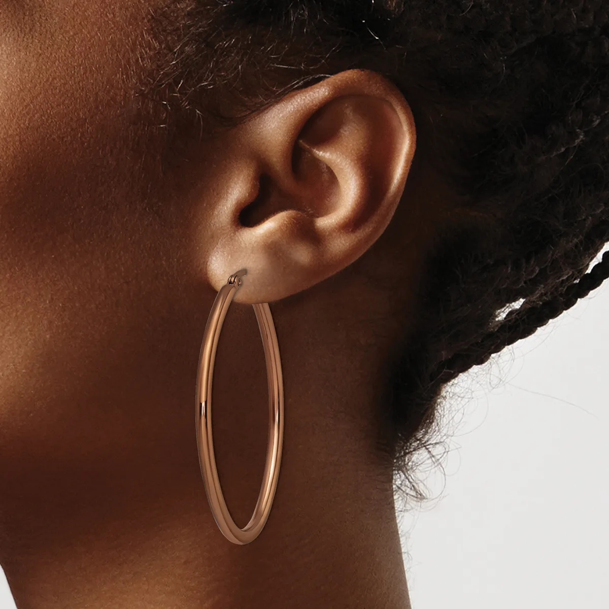 A person wearing a large oval hoop earring in rose gold or copper tone metal, shown in profile against a neutral background.