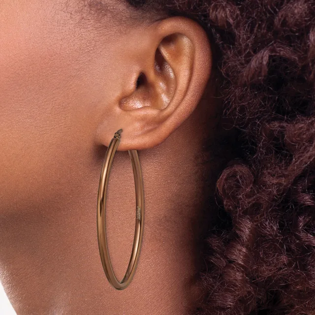 A person wearing large oval hoop earrings in a gold or brass-colored metal, shown in profile against dark curly hair.