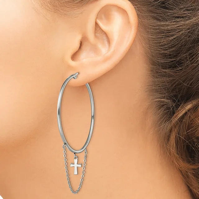 Silver-toned hoop earrings with dangling chain and small cross charms, worn on a person's ear.