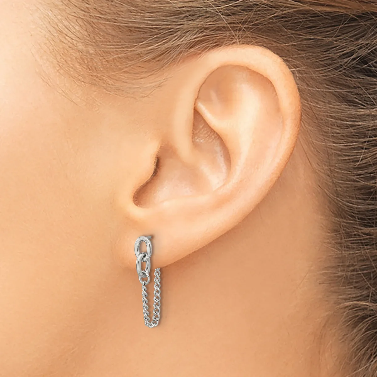 A silver chain hoop earring is worn in the pierced earlobe of a person with brown hair.