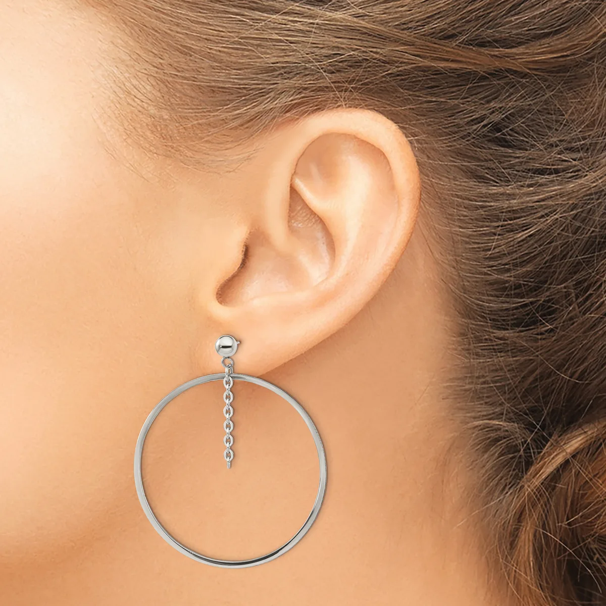 A woman wearing a large circular silver hoop earring with a delicate chain accent, shown from the side view of her ear and neck.
