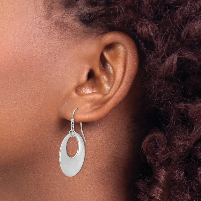 A person wearing a silver oval drop earring with an open center, shown from the side view against their ear and dark curly hair.