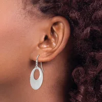 A person wearing a silver oval drop earring with an open center, shown from the side view against their ear and dark curly hair.