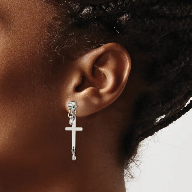 A person wearing a silver cross pendant earring with a chain attachment, shown from the side view of their ear and neck.