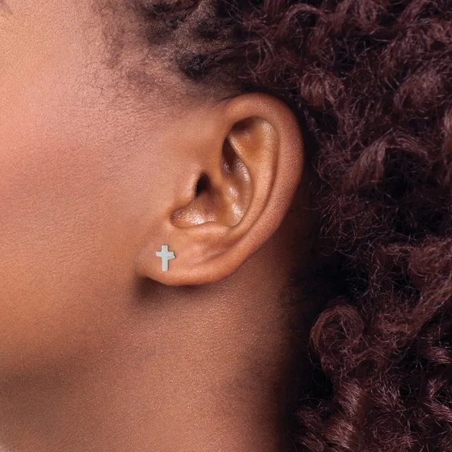 A person with dark curly hair wearing a small silver cross stud earring in their earlobe.