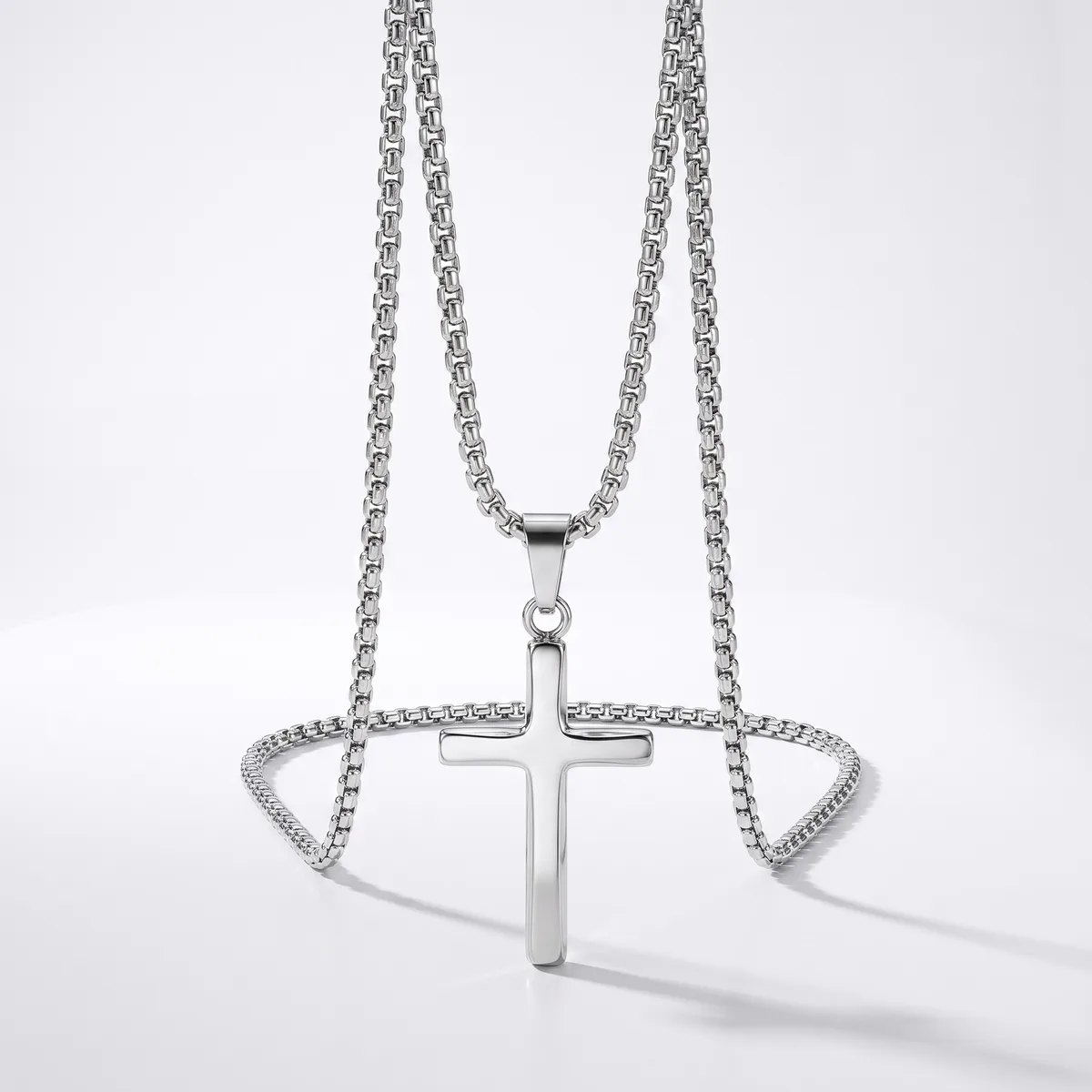 Silver-toned chain necklace with a polished cross pendant and matching decorative chain bracelet displayed on a white background.