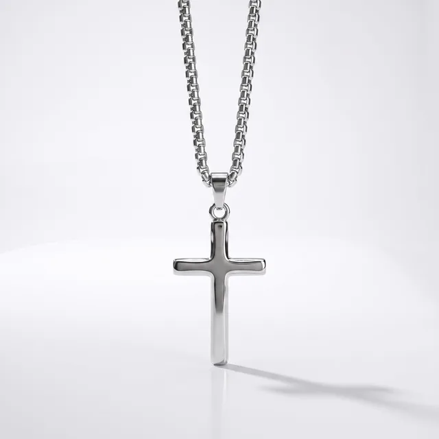A polished silver cross pendant hangs from a matching chain against a white background, casting a soft shadow.