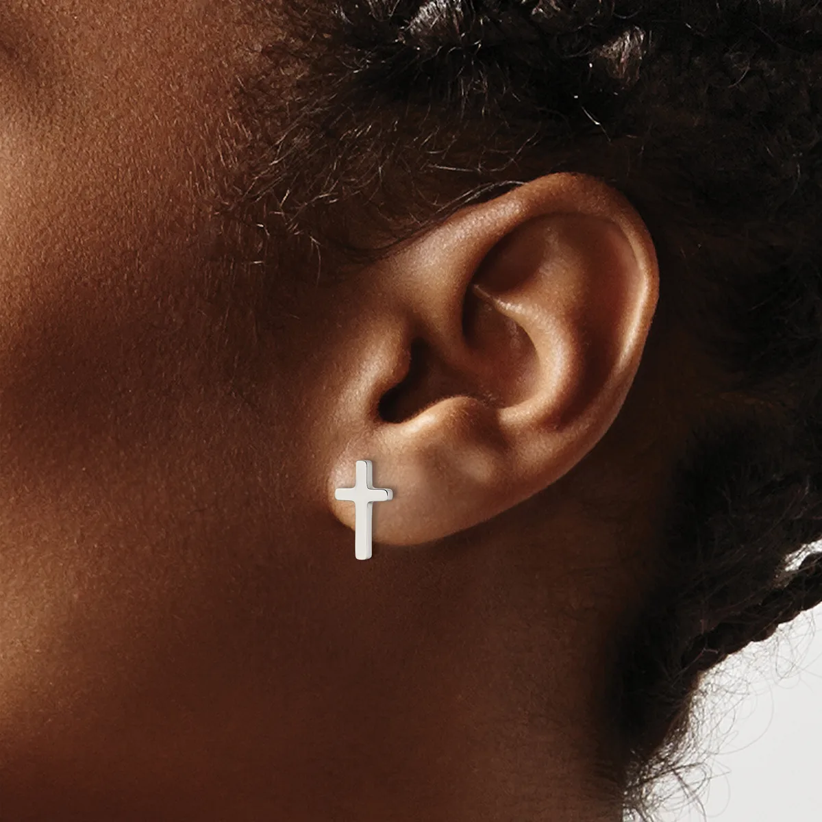 A white cross-shaped earring worn on the earlobe of a person with brown skin and dark hair.