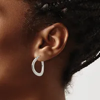 A person wearing a silver hoop earring in their pierced earlobe, shown in profile against a white background.