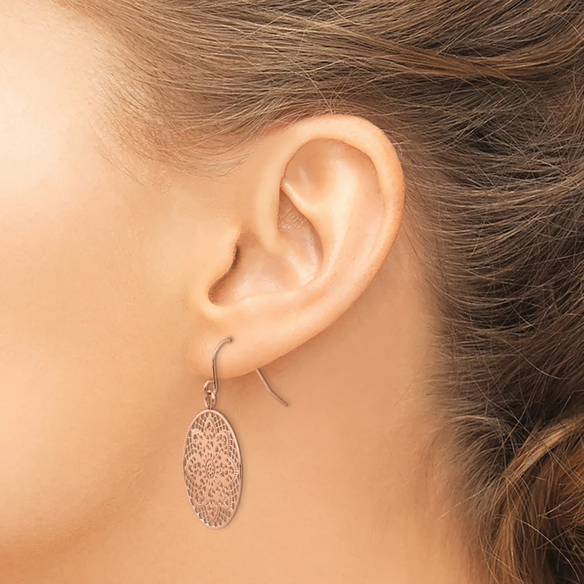A person wearing a textured oval pendant earring on a curved ear wire, shown from the side view against their neck and shoulder.