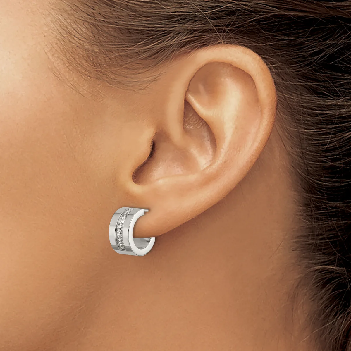 A silver hoop earring with a textured band worn on a person's earlobe, shown in profile view.