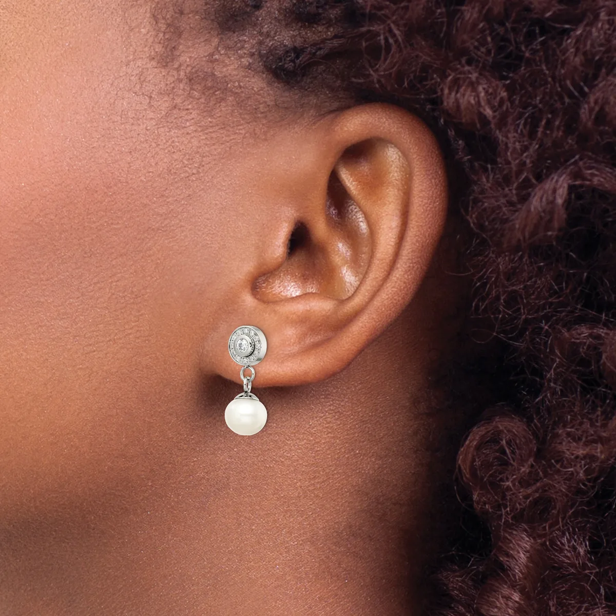 A person wearing a dangling earring with a round blue stone on top connected to a white pearl drop, shown from the side view against their ear.