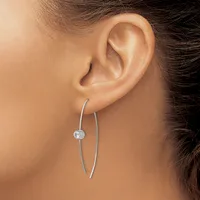 A person wearing long curved silver earrings with a small round white stone accent on one earring, shown from the side view of their ear and neck.