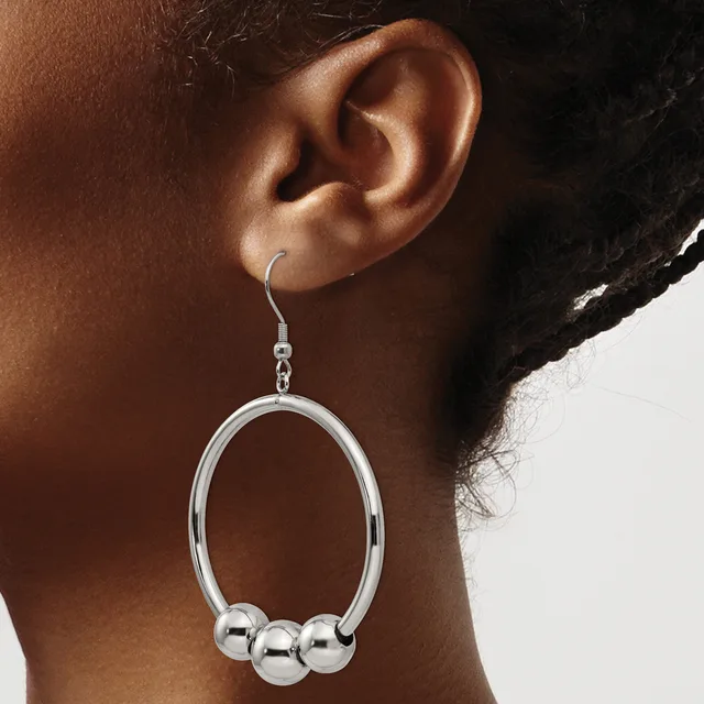A person wearing a silver-toned oval dangle earring with three spherical beads suspended from a hook closure.