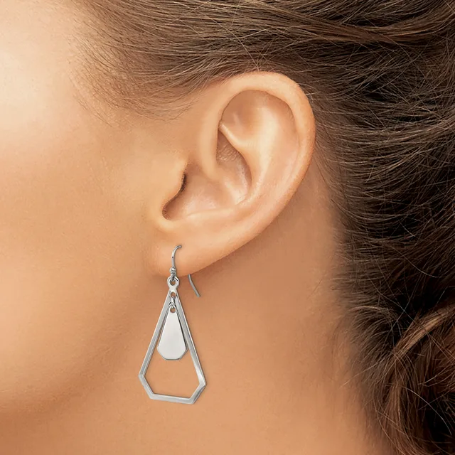 A person wearing a silver geometric teardrop-shaped dangle earring with a hollow pentagonal outline, shown from the side view of their ear.