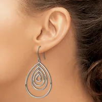 A woman wears silver teardrop-shaped dangle earrings with concentric nested outlines on hook-style ear wires.