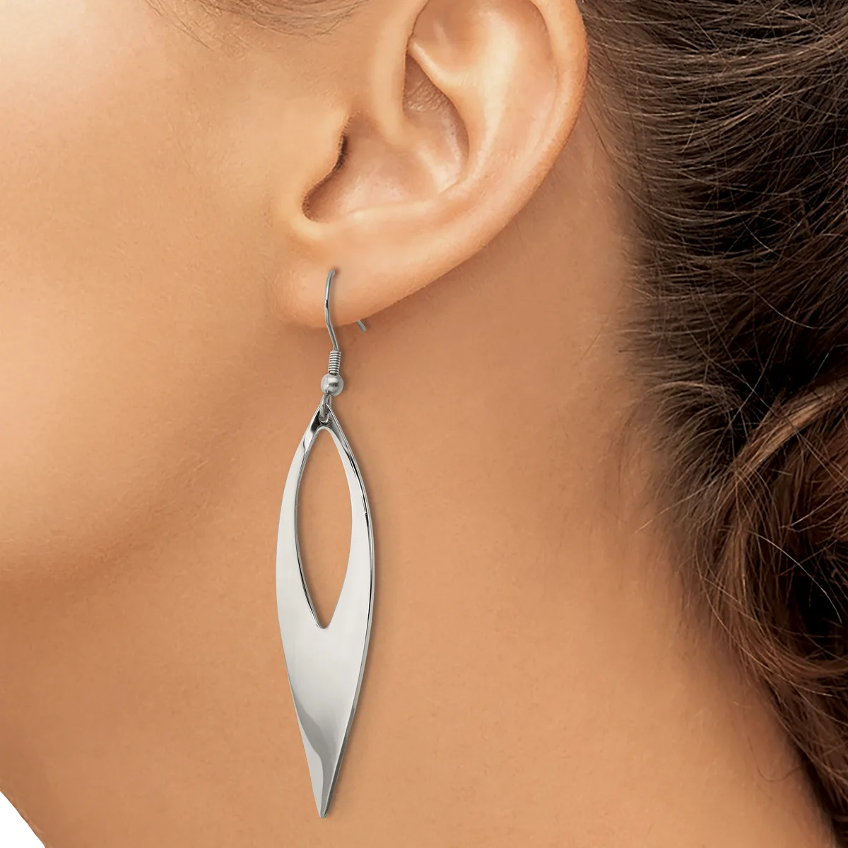 A woman wearing a long, slender silver drop earring with an elongated oval cutout design, shown hanging from her earlobe.