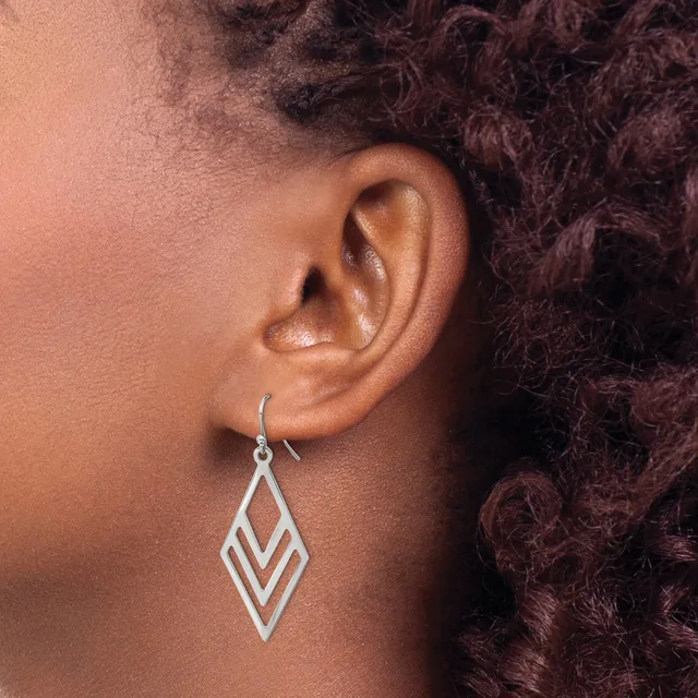 A silver geometric diamond-shaped dangle earring with nested chevron cutouts hangs from an ear lobe.