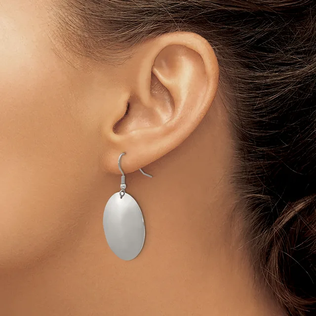 A person wearing a silver oval drop earring on a fish hook wire, shown from the side view of their ear and neck.