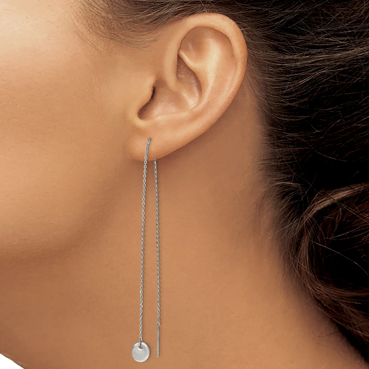 A person wearing a long silver chain threader earring with a small disc pendant hanging from the earlobe.