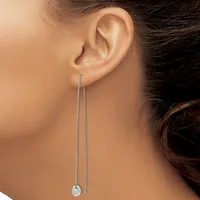 A person wearing a long silver chain threader earring with a small disc pendant hanging from the earlobe.