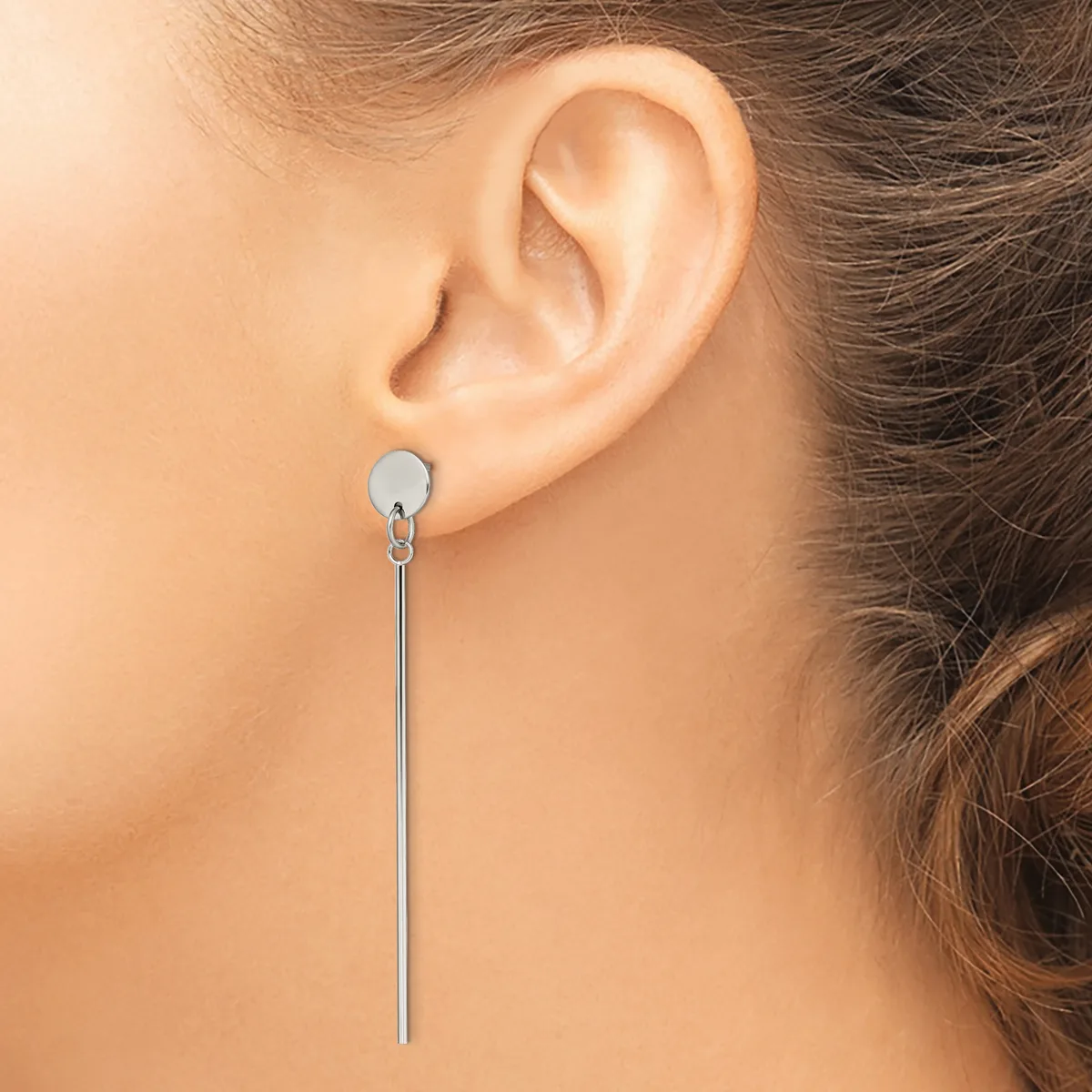 A woman wearing a long silver threader earring with a small disc top hanging from her pierced earlobe.
