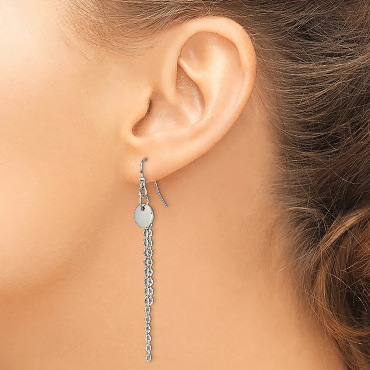 A person wearing a long silver chain earring with a small circular disc at the top, shown from the side view of their ear.