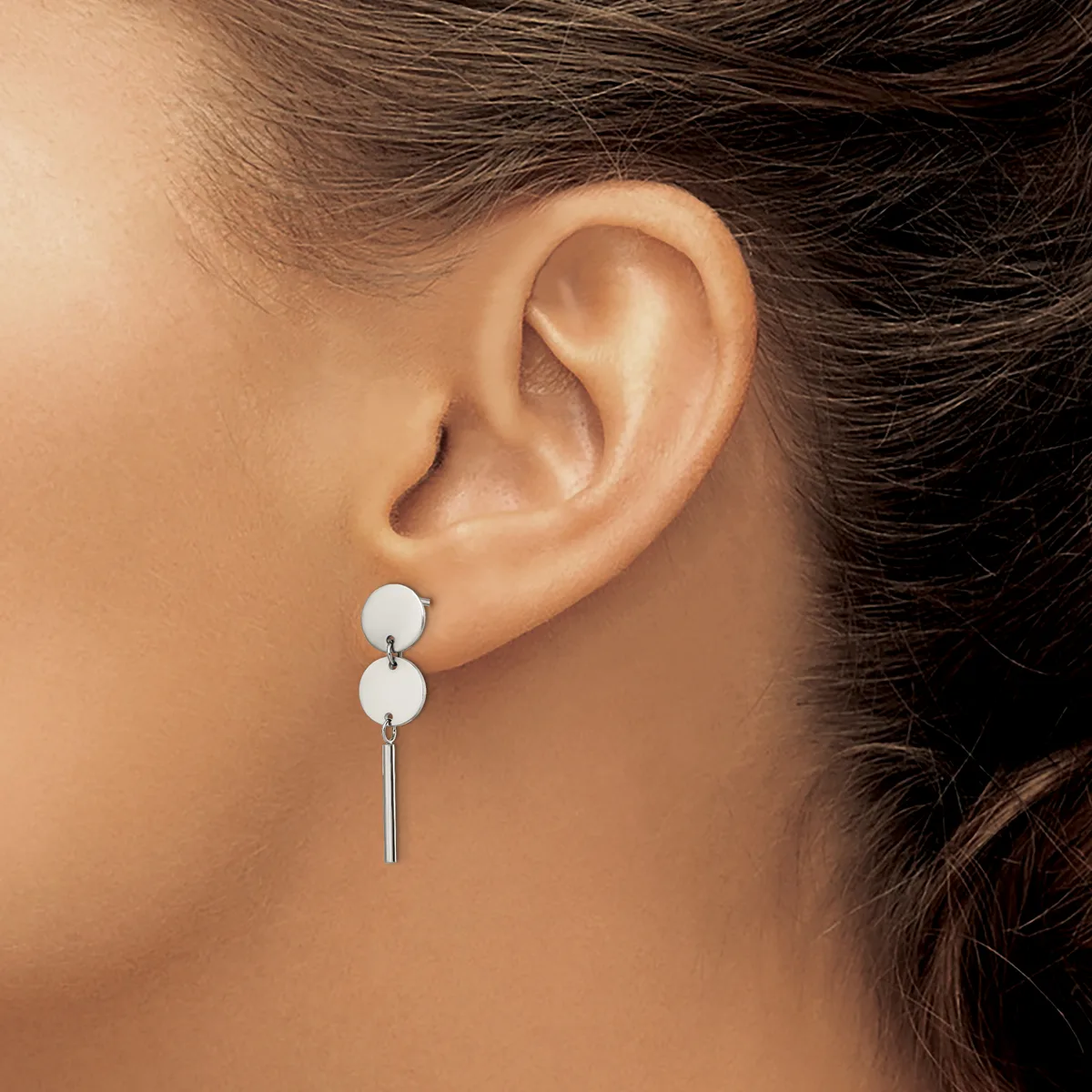 A woman wearing a pair of silver drop earrings with two white spheres stacked vertically and a thin bar hanging below, shown from the side view of her ear and neck.