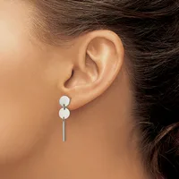 A woman wearing a pair of silver drop earrings with two white spheres stacked vertically and a thin bar hanging below, shown from the side view of her ear and neck.