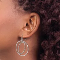 A person wearing a pair of silver-toned double oval hoop earrings with a hook closure, shown from the side profile against their ear and dark curly hair.