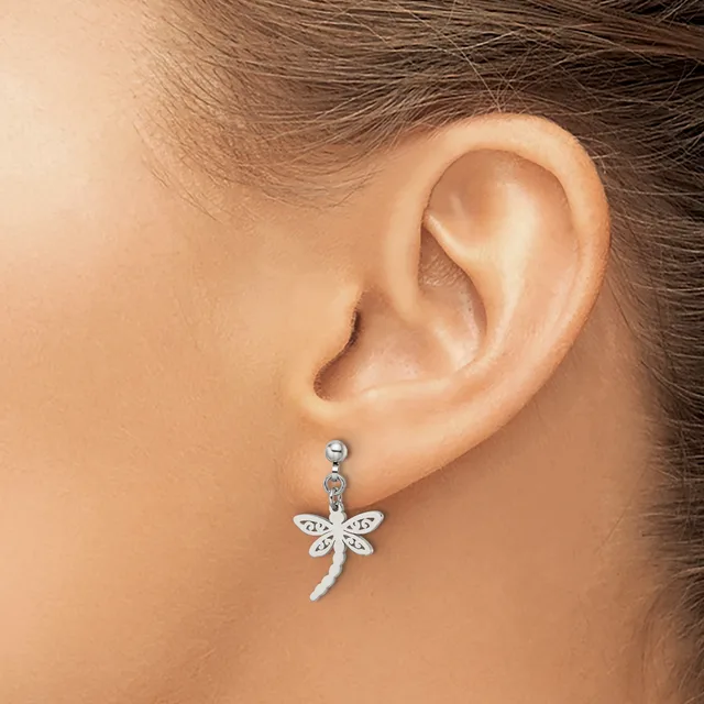 A person wearing a silver dragonfly pendant earring with textured wings hanging from a small round stud on their earlobe.