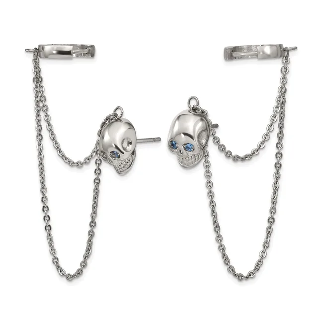 Silver skull stud earrings with blue stone eyes connected by chain drapes to bar ear cuffs.