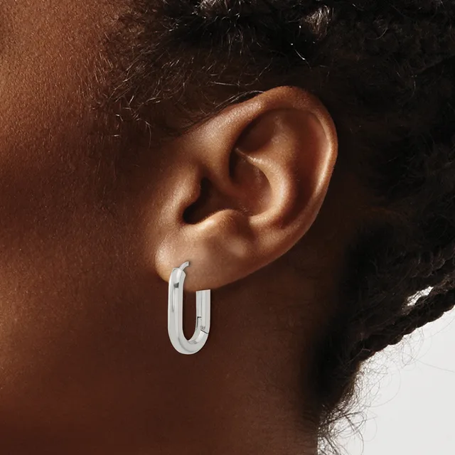 A person wearing a pair of polished silver rectangular hoop earrings with rounded corners, shown from the side profile.