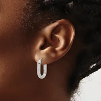 A person wearing a pair of polished silver rectangular hoop earrings with rounded corners, shown from the side profile.