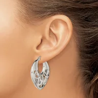 A woman wearing a silver hoop earring with a cutout leaf or feather pattern, shown from the side view of her ear and neck.