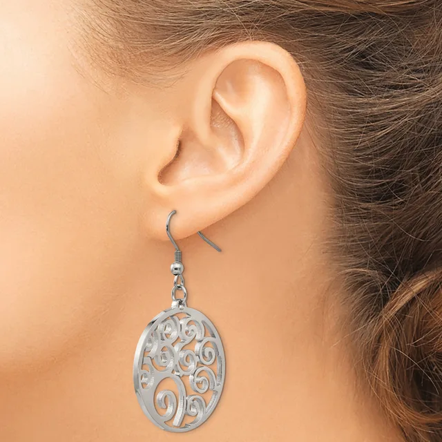 A silver-toned filigree oval dangle earring with scrollwork cutout design hangs from a fish hook wire on a person's earlobe.