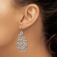 A woman wearing a silver filigree drop earring with an ornate scrollwork design hanging from a curved wire hook.