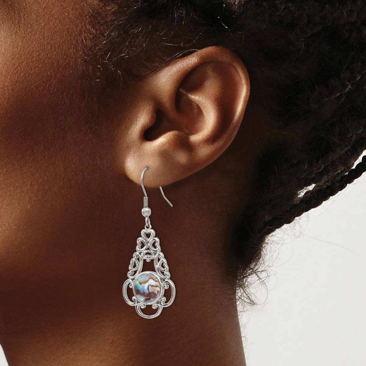 A person wearing a silver-toned filigree teardrop earring with an iridescent stone center, shown hanging from the earlobe.