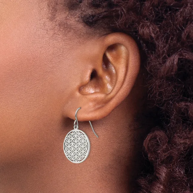 A person wearing a silver drop earring with an oval pendant featuring a geometric flower of life pattern, shown from the side view against their ear and shoulder.