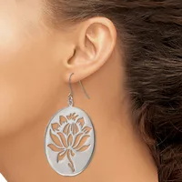 A person wearing a silver oval dangle earring with a cutout lotus flower design in the center, suspended from a curved wire hook.