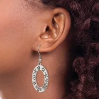 A silver oval dangle earring with decorative filigree patterns hangs from a person's earlobe.