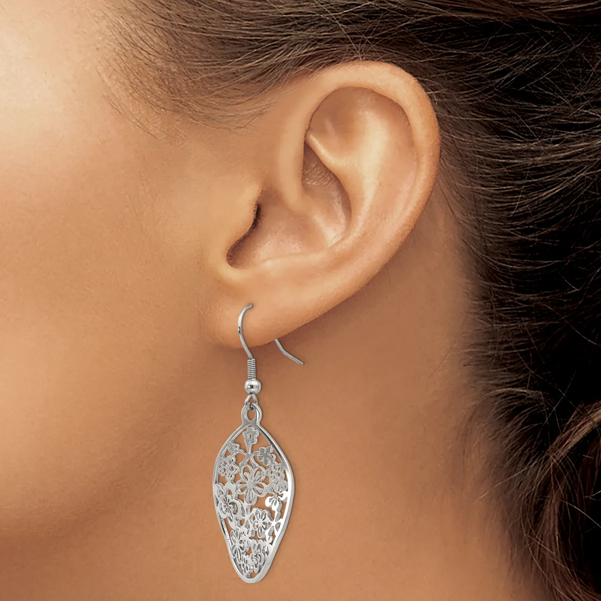 A woman wearing a silver filigree leaf-shaped dangle earring with an ornate cutout pattern, shown from the side view of her ear and face.