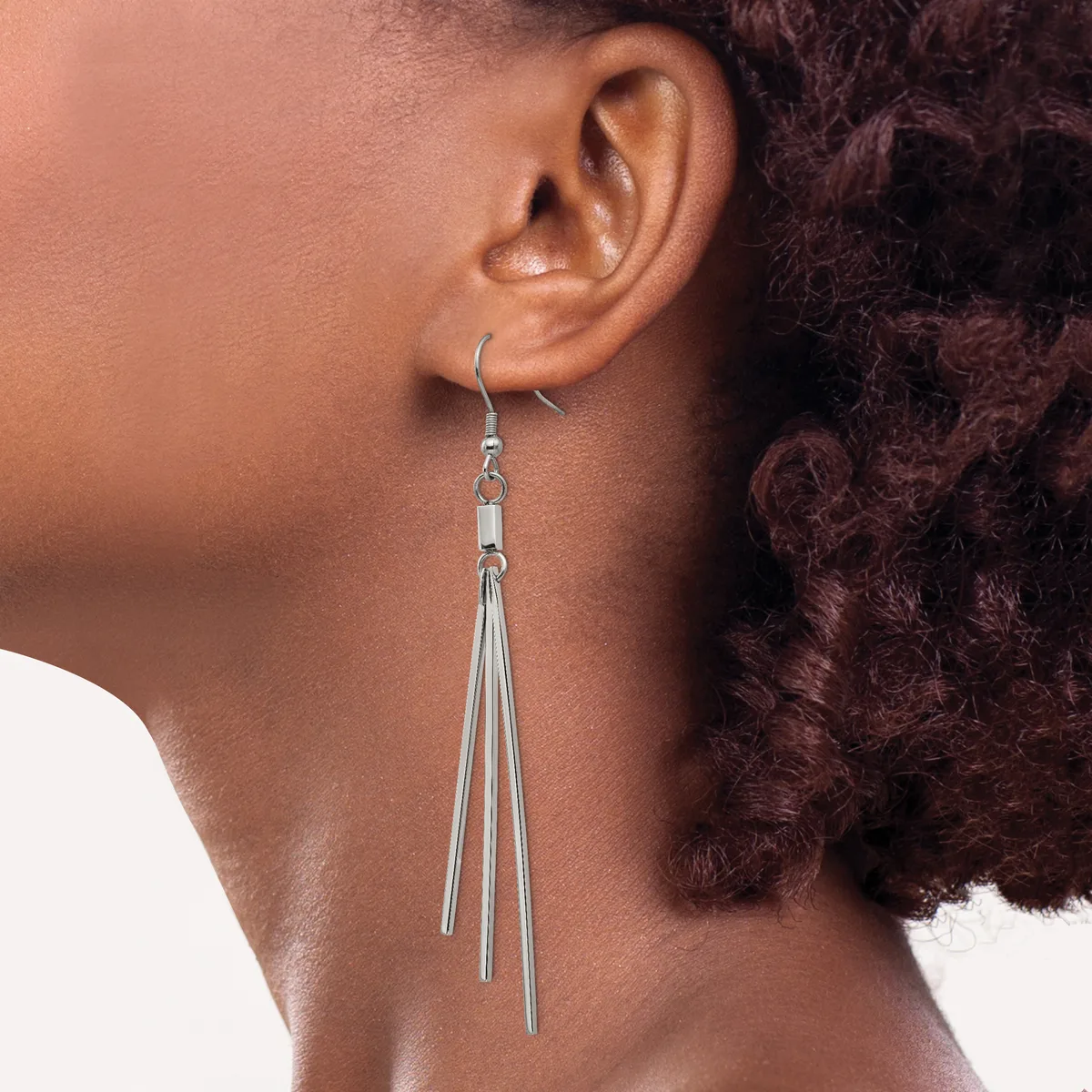 A person wearing a long tapered silver dangle earring with multiple thin strands hanging from a hook fastening, shown from the side profile.