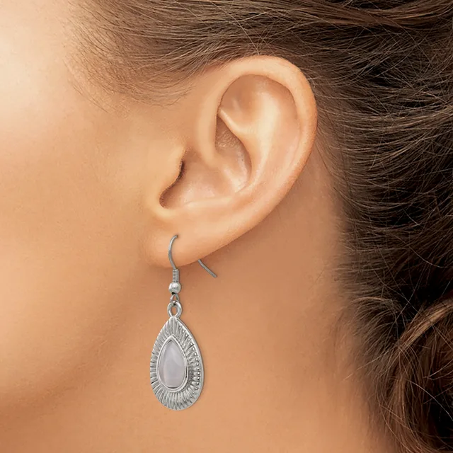 A woman wearing a teardrop-shaped silver earring with a white stone center and textured border, suspended from a silver ear wire.