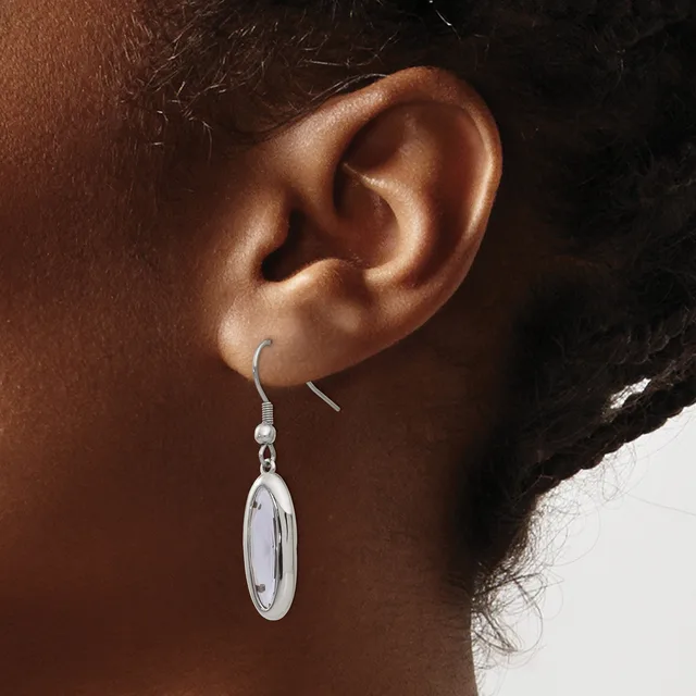 A silver oval dangle earring hangs from a fish hook wire on a person's earlobe.