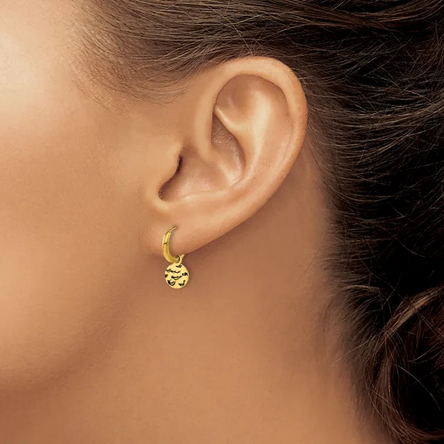 A person wearing a gold hoop earring with a small decorative charm pendant hanging from it, shown from the side view of their ear.