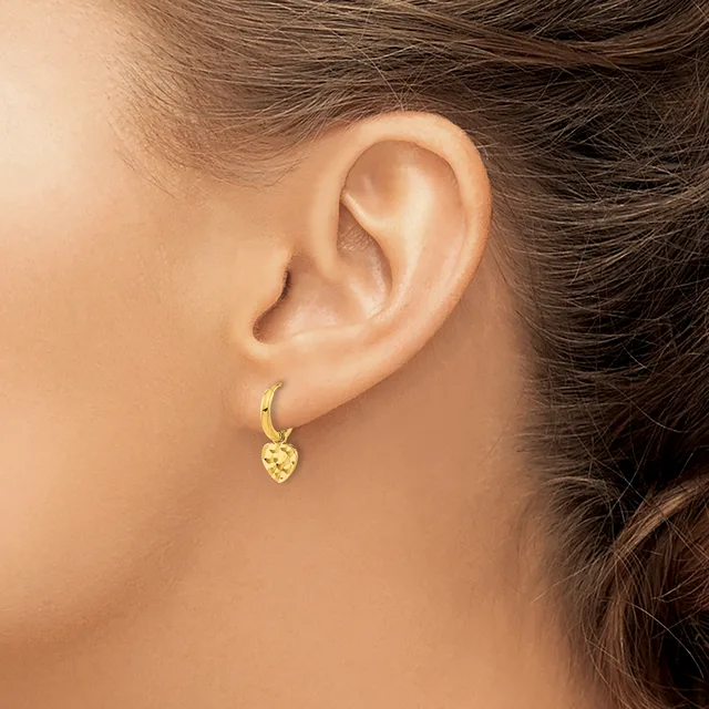 A person wearing a gold hoop earring with a small textured heart charm dangling from it, shown from the side profile of their ear.