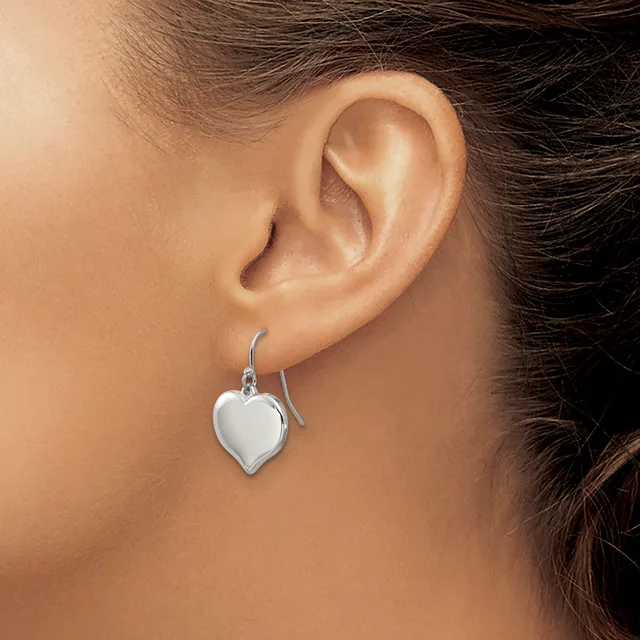A person wearing a silver heart-shaped dangle earring on a fish hook wire, shown from the side profile of their ear and neck.